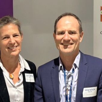 Dr Kathy Witt and Warwick Squire standing together in front of University of Queensland and Coexistence Queensland banners.
