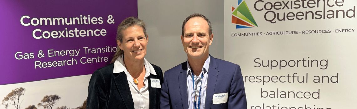 Dr Kathy Witt and Warwick Squire standing together in front of University of Queensland and Coexistence Queensland banners.